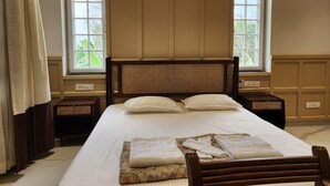 A neatly made bed with a headboard, two bedside tables, and a window with a view of greenery.