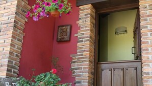 A brick building with a wooden door, a hanging flower basket, and a planter with plants.