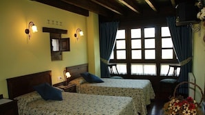 A room with two beds, a wooden ceiling, a window with curtains, and a wall-mounted light fixture.