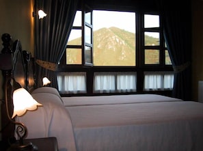 Et soveværelse med seng, natbord, lampe og et vindue med gardiner.