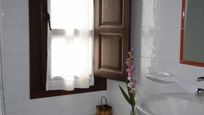 A bathroom with a white sink, a mirror, a window with a wooden frame, and a vase with flowers.