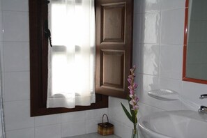 A bathroom with a white sink, a mirror, a window with a wooden frame, and a vase with flowers. - Casa Rural El Trechal (Pilona)