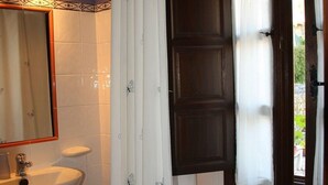 A bathroom with a white sink, a bathtub, a shower curtain, and a window with curtains.