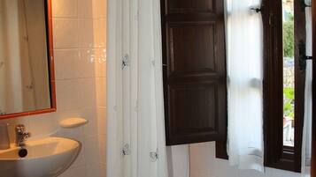 A bathroom with a white sink, a bathtub, a shower curtain, and a window with curtains.