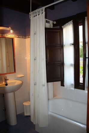 A bathroom with a white sink, a bathtub, a shower curtain, and a window with curtains. - Casa Rural El Trechal (Pilona)