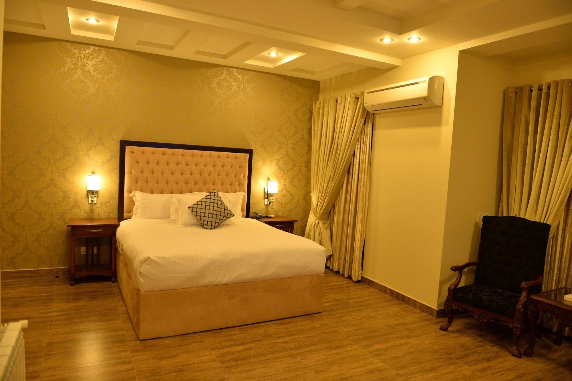 A hotel room with a large bed, two bedside lamps, an air conditioning unit, and a wooden chair.