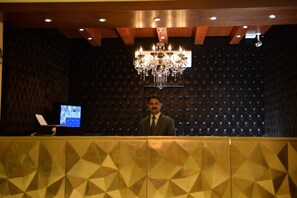 A reception desk with a geometric patterned design, a chandelier, and a television screen. - Bella View Lounge (Islamabad)