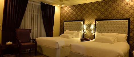 A hotel room with two beds, a chair, a ceiling fan, and patterned wallpaper.