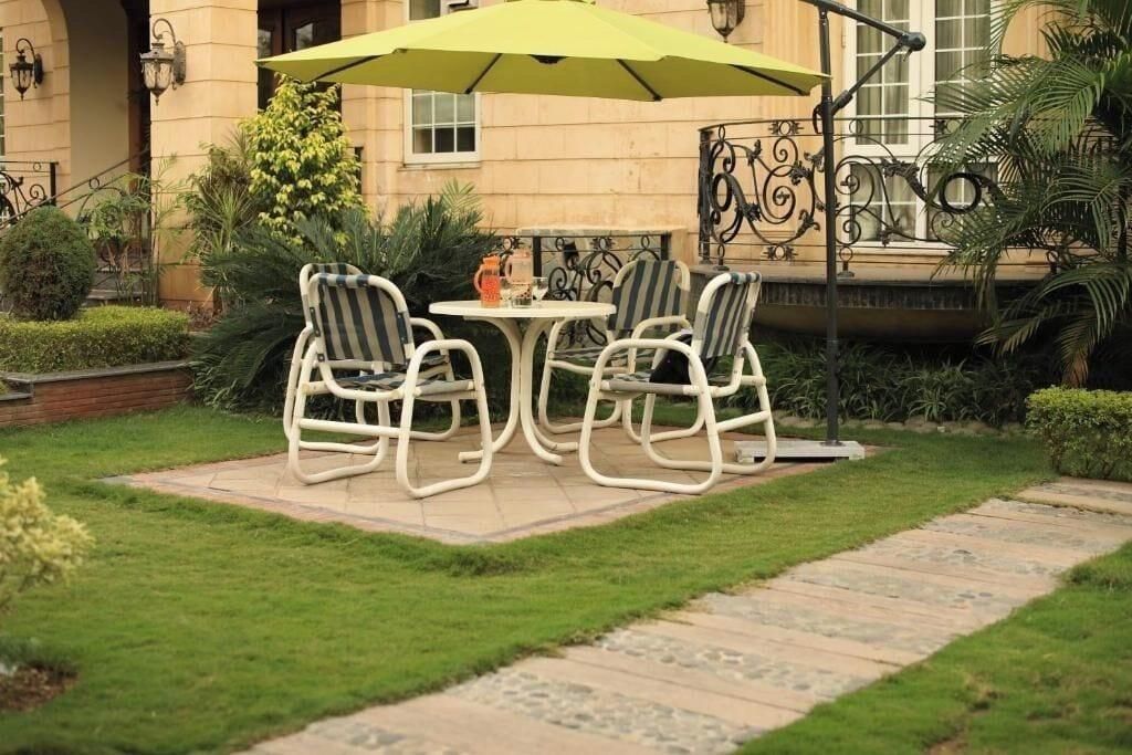 An outdoor seating area with a table and chairs, a green umbrella, and a pathway.