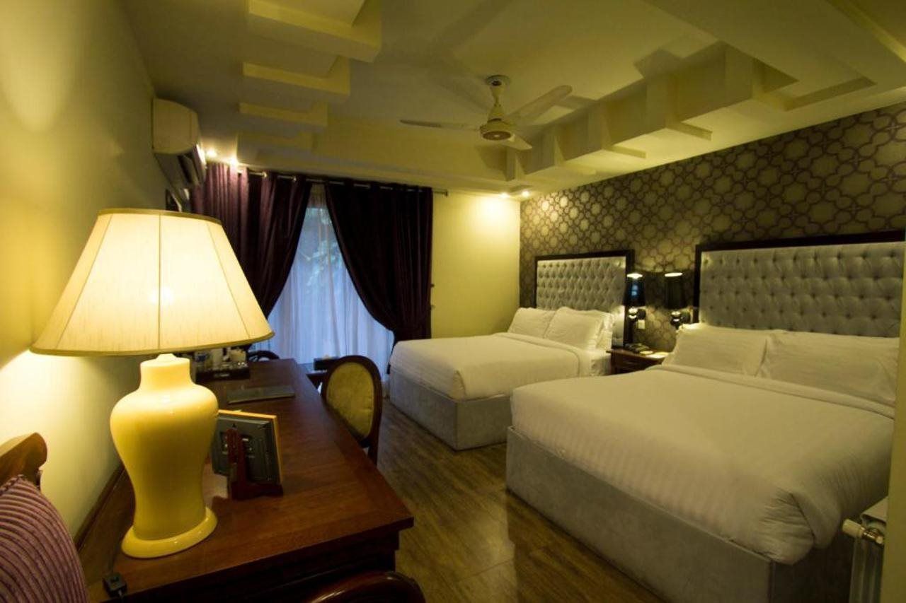 A hotel room with a bed, a desk with a lamp, a chair, and a window with curtains.