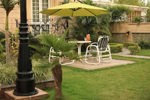 A patio with a table and chairs, a yellow umbrella, and a decorative lamp post. - Bella View Lounge (Islamabad)