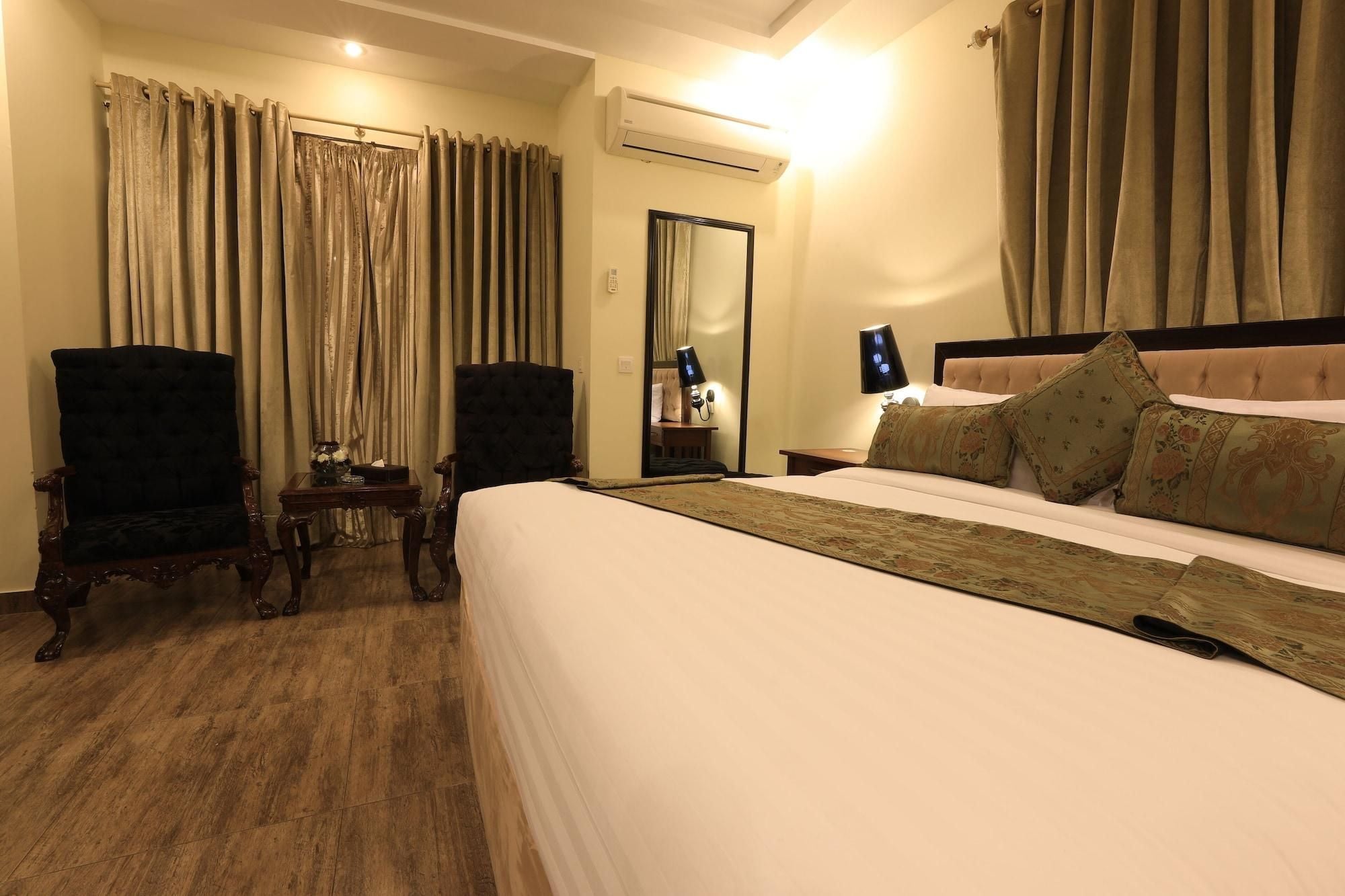 A hotel room with a bed, two armchairs, a bedside table, a mirror, and an air conditioning unit.