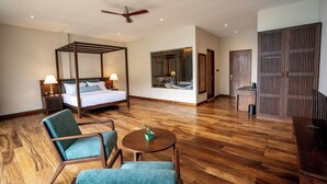 Una habitación de hotel con cama con dosel, una zona de estar con una mesa redonda y un ventanal grande.