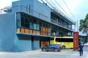 A modern building with a glass facade, a bus parked in front, and a man walking by. - Oak Ray Tea Bush Ramboda (Ramboda)