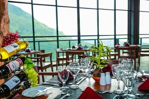 A dining table set with wine bottles, glasses, and a potted plant, overlooking a mountainous landscape. - Oak Ray Tea Bush Ramboda (Ramboda)