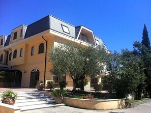 A multi-story building with a courtyard, a covered entrance, and a prominent tree. - Hotel Del Sole (Sora)