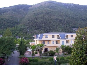 A two-story building with a sloped roof, surrounded by greenery and a mountain in the background. - Hotel Del Sole (Sora)
