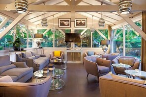 A modern interior with a high ceiling, large windows, and a central seating area with sofas and tables. - Hotel Acadie Les Ulis (Villebon-sur-Yvette)
