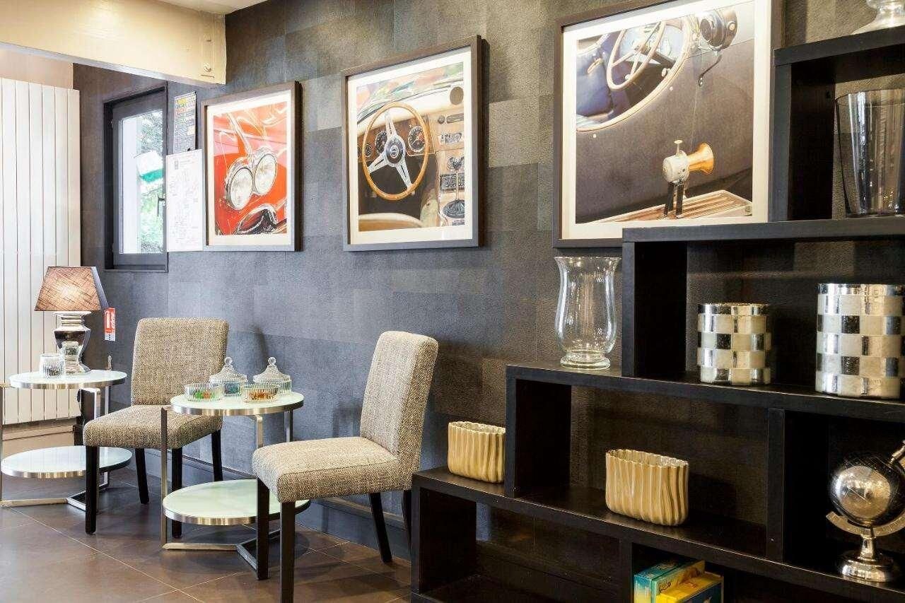 Una habitación con pared oscura, cuadros enmarcados, una lámpara y una estantería con objetos decorativos.