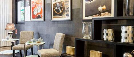 Una habitación con pared oscura, cuadros enmarcados, una lámpara y una estantería con objetos decorativos.