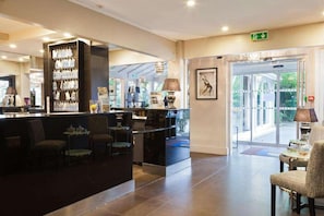 A hotel lobby with a reception desk, seating area, and a large glass door leading outside. - Hotel Acadie Les Ulis (Villebon-sur-Yvette)
