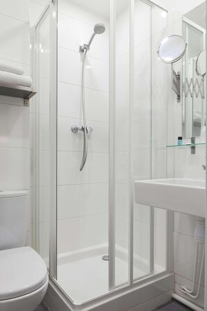 A glass-enclosed shower with a handheld showerhead, a white toilet, and a glass shelf above the sink. - Hotel Acadie Les Ulis (Villebon-sur-Yvette)