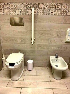 Un baño con inodoro, bidé y un cubo de basura.