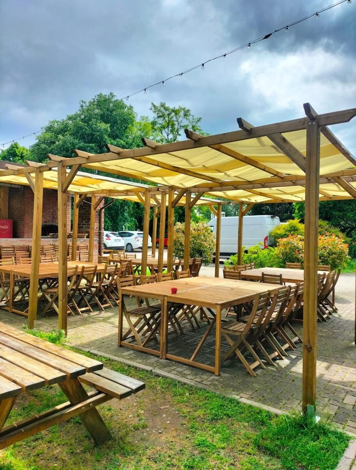 Un área de estar al aire libre con mesas y sillas de madera, cubierta por una pérgola con toldos amarillos.