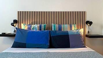 Un letto con testiera a righe, due comodini con lampade e asciugamani piegati sul pavimento.