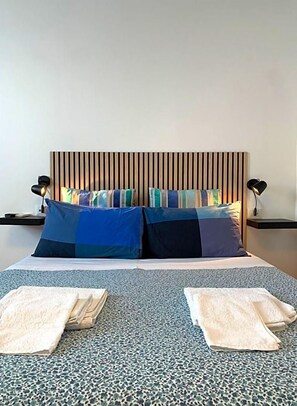 A bed with a striped headboard, two bedside tables with lamps, and folded towels on the floor. - Cascina Bellaria (Milan)