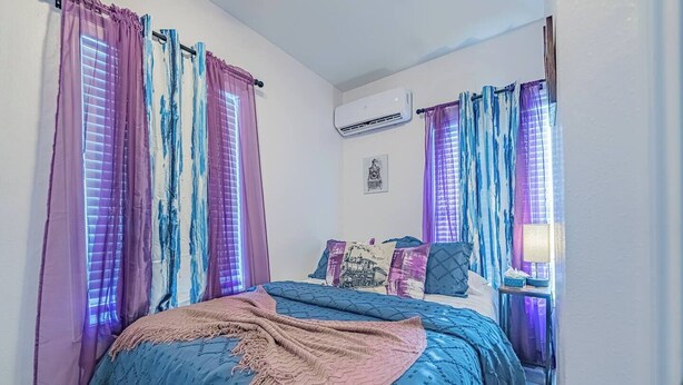 A bedroom with a bed, curtains, an air conditioning unit, and a wall-mounted picture. - Super Value Suite #6 - *4 km from FIFA Fan Fest* (Houston)