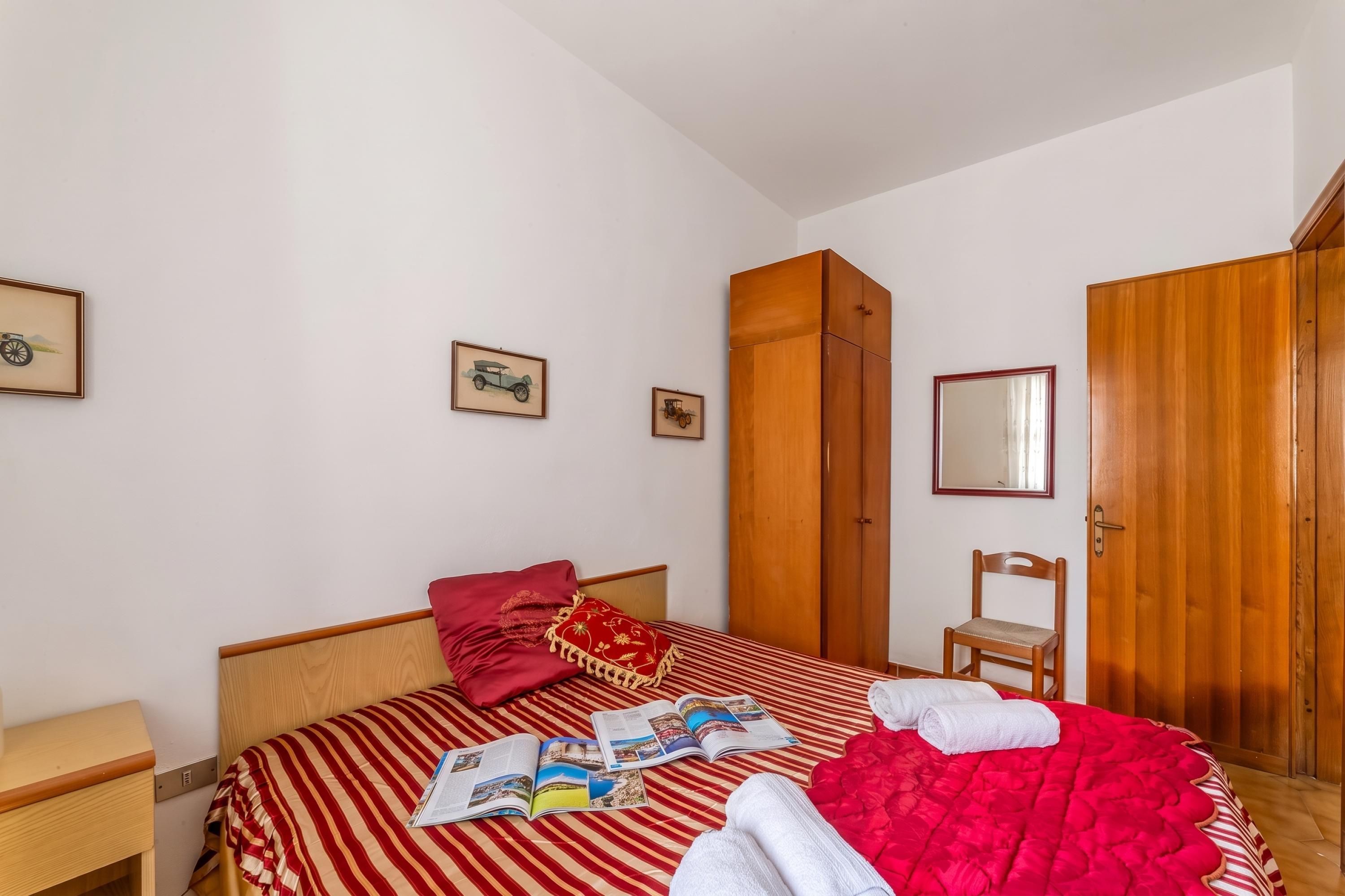 Ein Schlafzimmer mit einem Bett, einem Holzschrank, einem Sessel und einem Spiegel an der Wand.