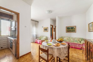 A dining area with a table set for two, a sofa, and a kitchen area with a stove and oven. - Leuca Relax&Sea n.2C, Castrignano del Capo, Italy (Castrignano del Capo)