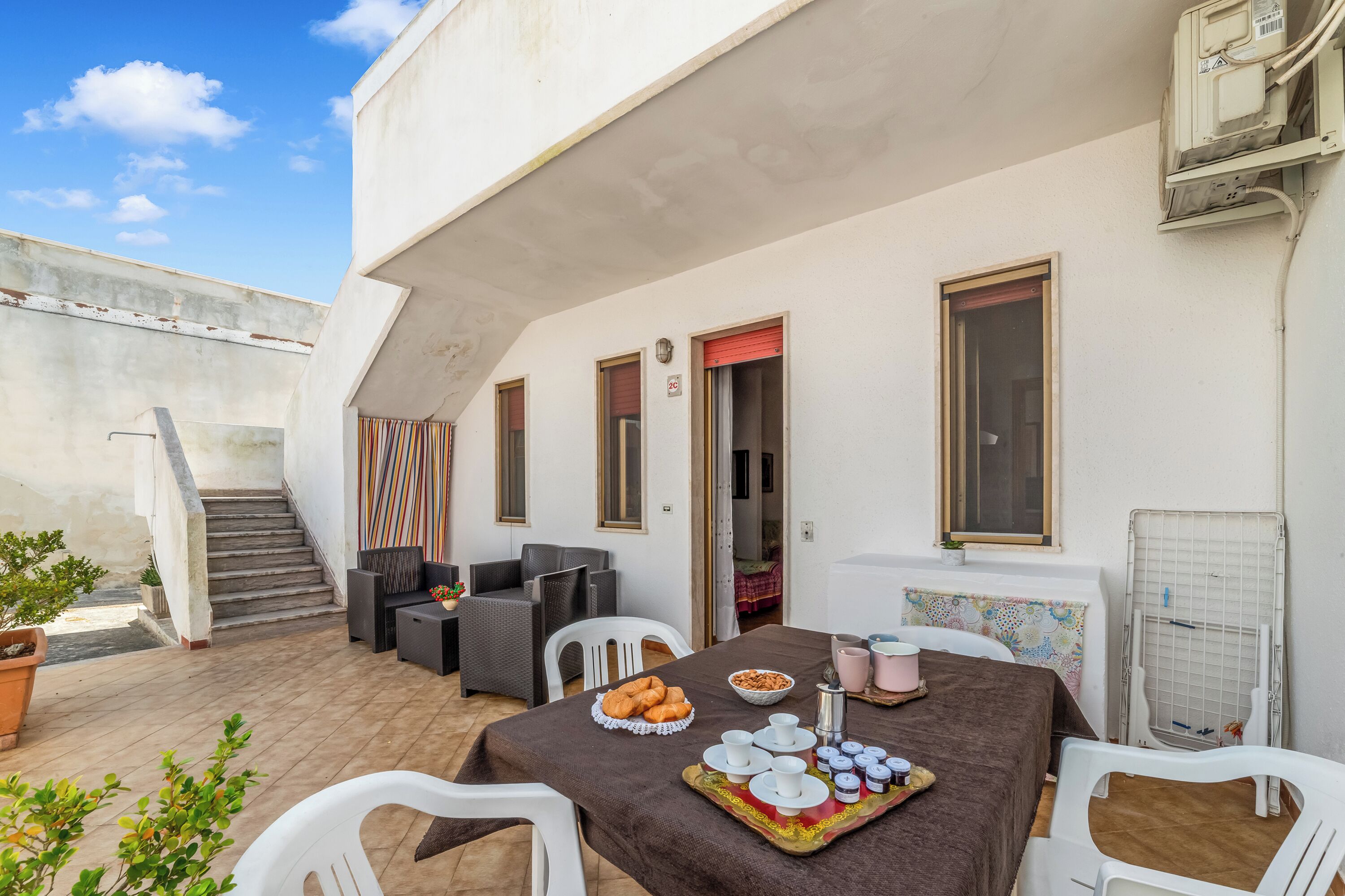 A patio with a dining table set for breakfast, outdoor seating, and a staircase leading to an upper level.