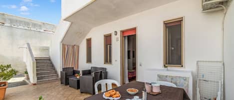 A patio with a dining table set for breakfast, outdoor seating, and a staircase leading to an upper level.