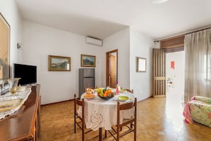 A dining area with a table set for four, a television, and a refrigerator in the background. - Leuca Relax&Sea n.2C, Castrignano del Capo, Italy (Castrignano del Capo)