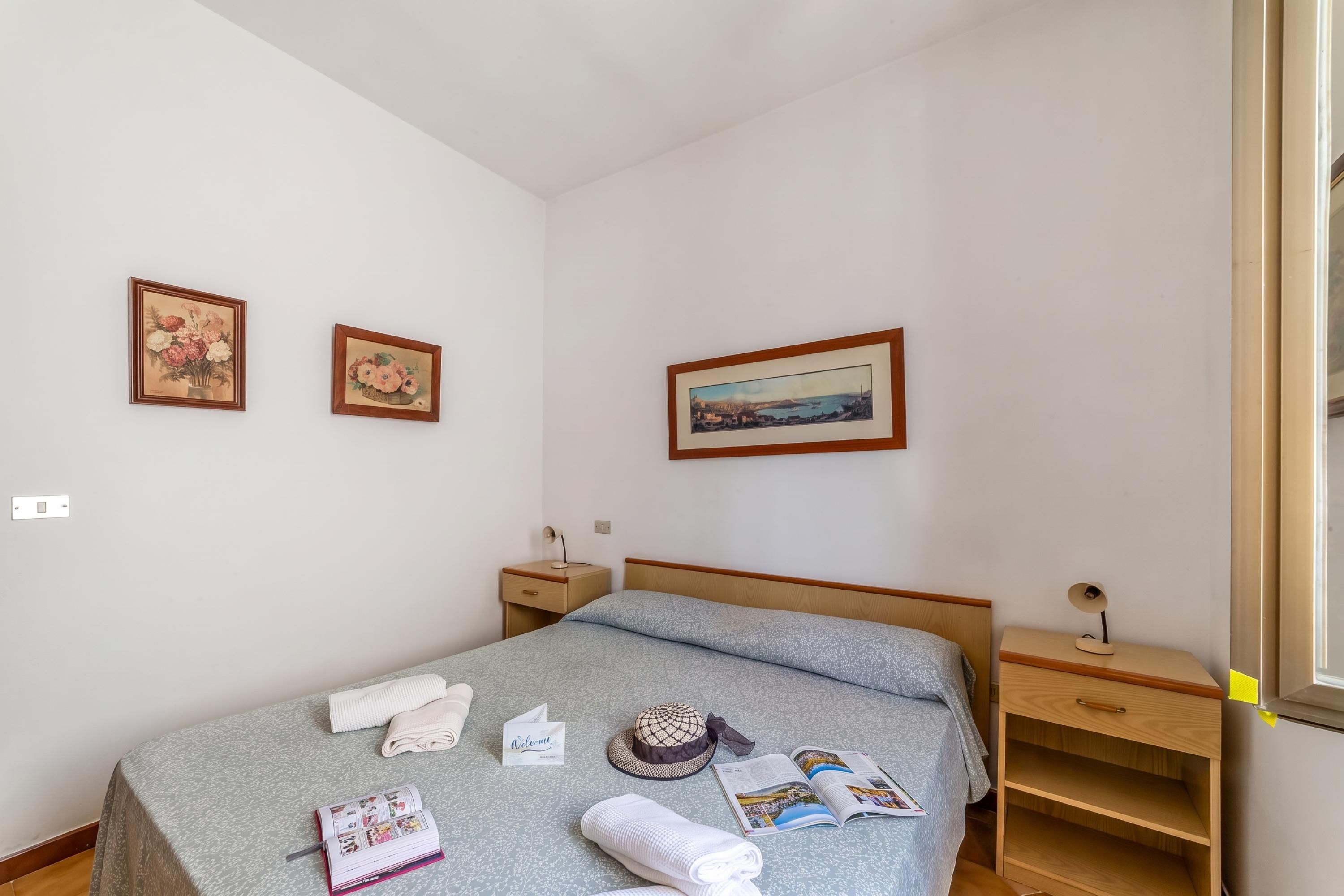 A neatly arranged bedroom with a bed, bedside tables, a nightstand, a window, and three framed pictures on the wall.