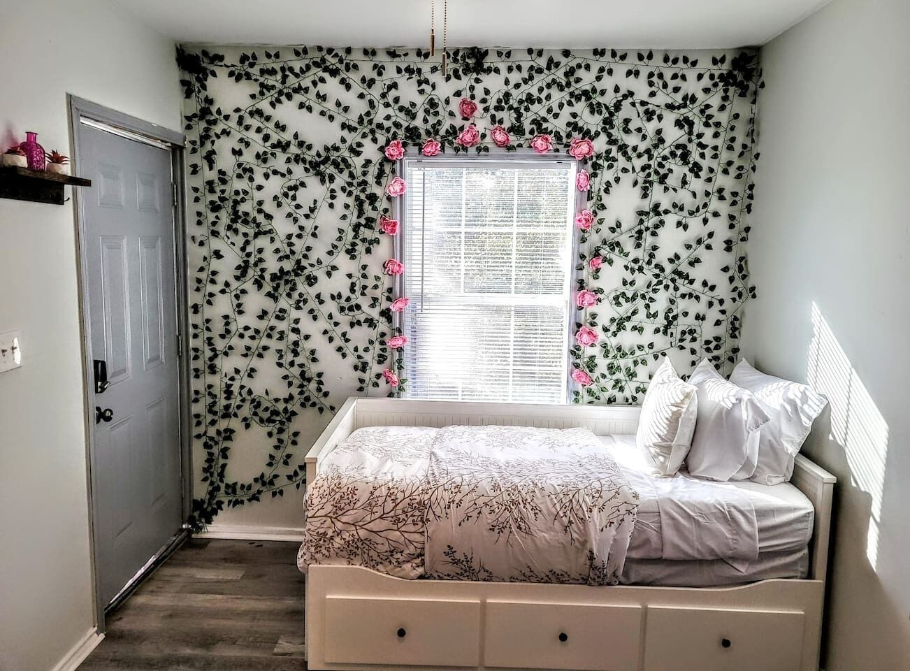 A bedroom with a bed, a window with a view, a door, and a wall with a leaf pattern.