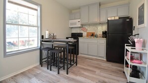 Une cuisine avec une fenêtre, un ventilateur de plafond, un four à micro-ondes, une cuisinière, un réfrigérateur et un meuble blanc.
