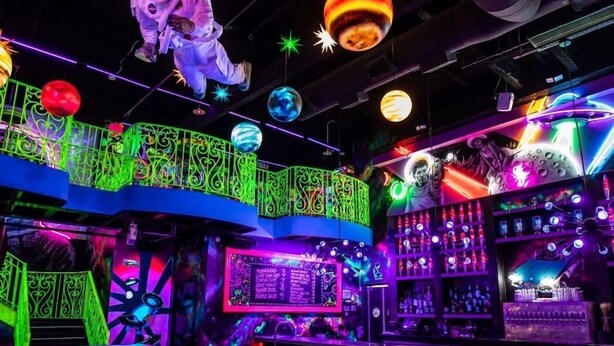 Un bar avec des néons, un barman et une enseigne lumineuse.