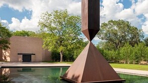 Une sculpture moderne dans une cour intérieure avec une piscine, entourée d’arbres et d’un bâtiment.