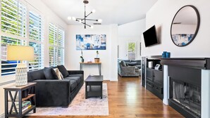 Un salon moderne avec un canapé noir, une table basse, une cheminée et un téléviseur fixé au mur.