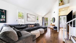 Un salon spacieux avec un grand canapé d’angle, des poufs, un téléviseur à écran plat et un escalier menant à un niveau supérieur.
