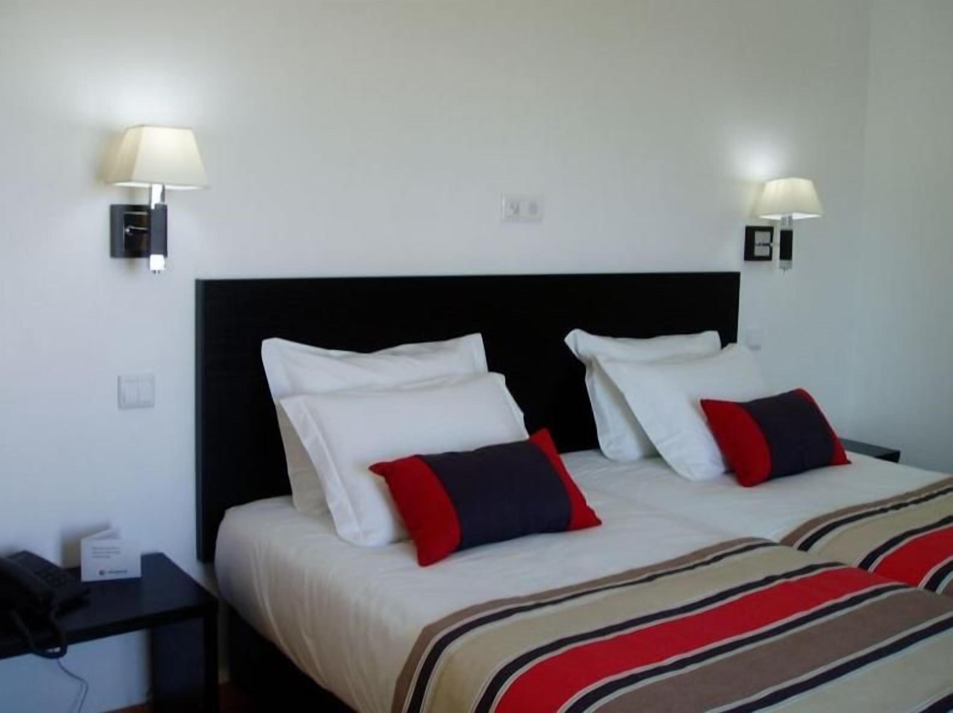 A hotel room with a double bed, two bedside tables, and two wall-mounted lamps.