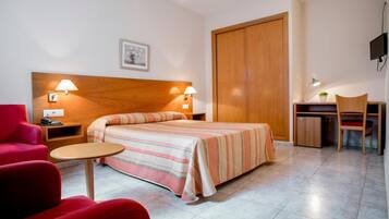 Una habitación de hotel con una cama, un escritorio, una silla, un sillón rojo y un televisor.