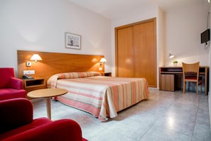 Una habitación de hotel con una cama, un escritorio, una silla, un sillón rojo y un televisor.