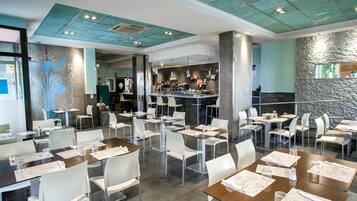 Un restaurante con varias mesas y sillas, una zona de bar y un mostrador de recepción.