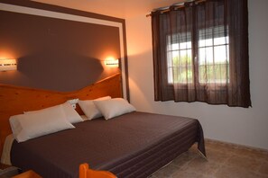 A bedroom with a wooden headboard, a large bed with a brown bedspread, two pillows, a nightstand, and a window with curtains. - Hotel Restaurante Las Camelias (Coana)