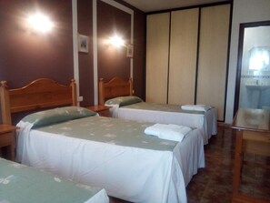 A hotel room with two single beds, a wooden headboard, a bedside table, and a large window.