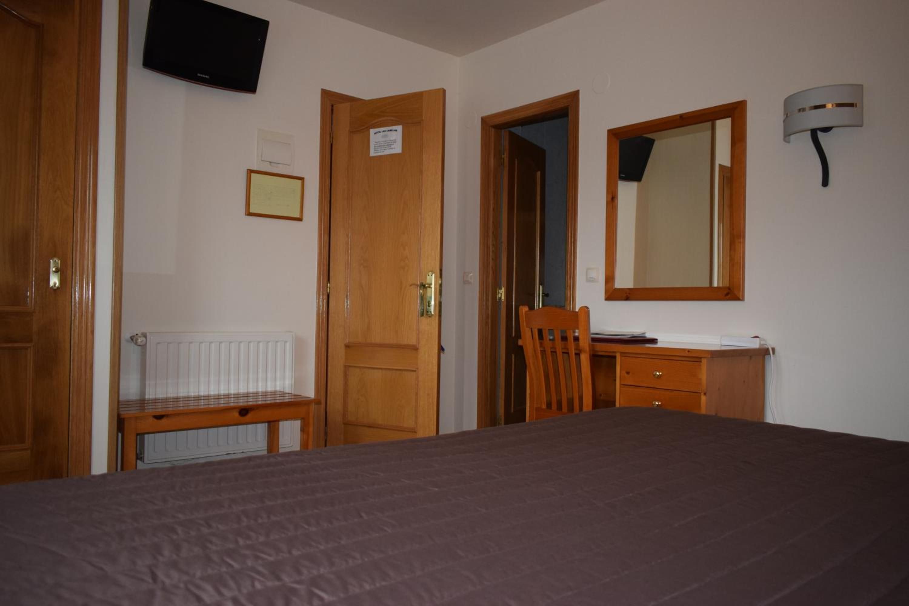 Una habitación de hotel con cama, escritorio con silla, radiador, televisor montado en la pared y espejo.